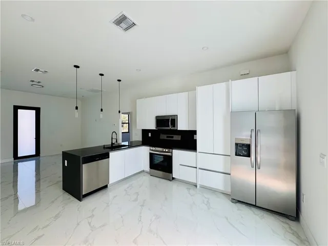 Kitchen featuring stainless steel appliances, pendant lighting, white cabinets, light marble finish floors, and a peninsula