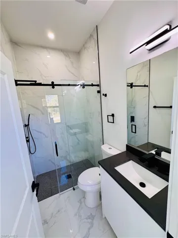 Full bath featuring vanity, light marble finish flooring, and a marble finish shower