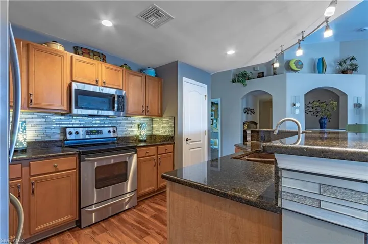 Kitchen with sink, dark stone countertops, appliances with stainless steel finishes, dark hardwood / wood-style floors, and backsplash
