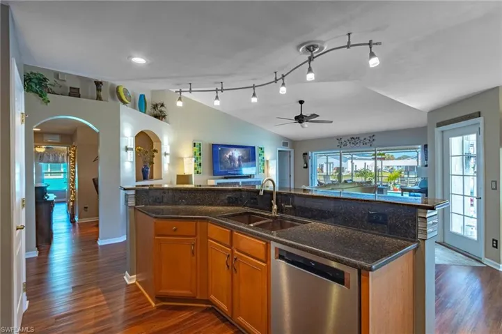 Kitchen with a kitchen island with sink, sink, stainless steel dishwasher, and dark stone counters