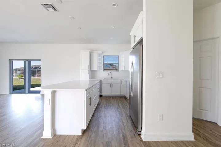 Kitchen with stainless steel refrigerator, a kitchen island, wood-type flooring, white cabinets, and sink