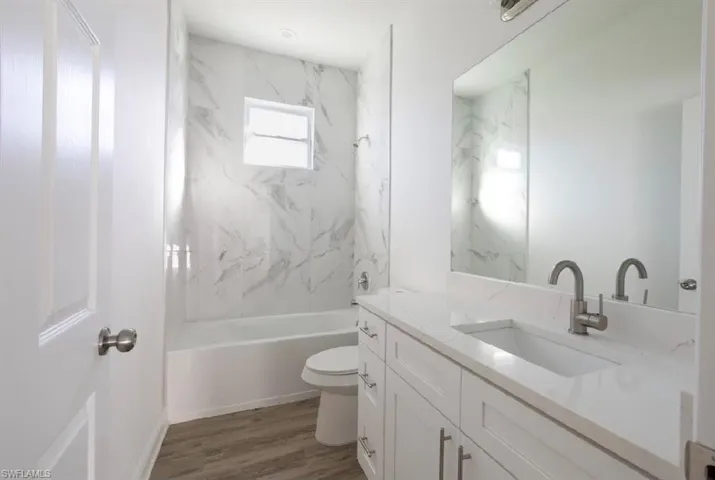 Full bathroom featuring hardwood / wood-style flooring, tiled shower / bath combo, vanity, and toilet