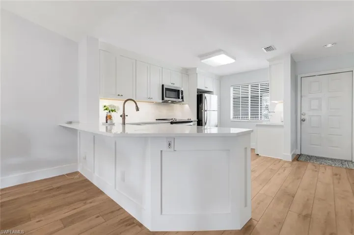 Kitchen with a peninsula, white cabinets, light wood-style floors, and stainless steel appliances