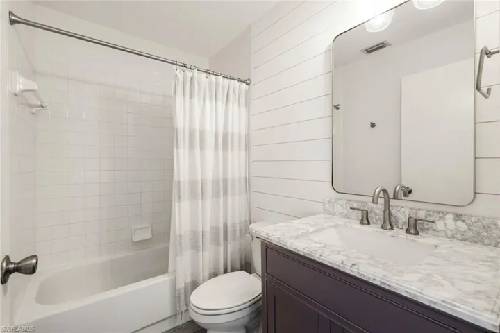 Bathroom with shower / bathtub combination with curtain, vanity, and wooden walls