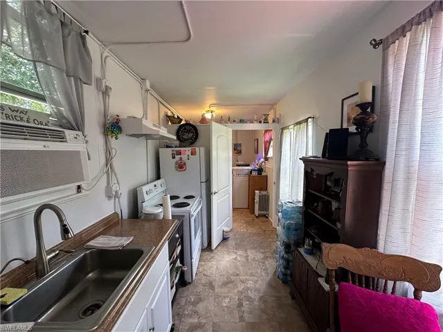 Kitchen with white appliances, white cabinets, radiator heating unit, and under cabinet range hood