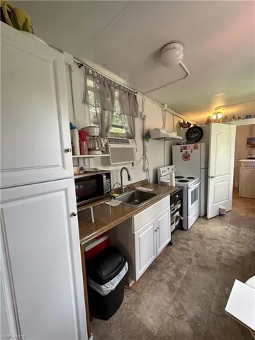 Kitchen with white appliances, white cabinetry, washer / clothes dryer, under cabinet range hood, and cooling unit