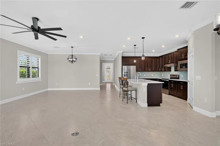 Kitchen featuring a kitchen breakfast bar, dark brown cabinetry, a center island with sink, crown molding, and stainless steel appliances
