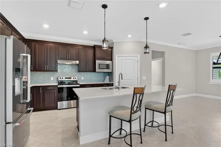 Kitchen with stainless steel appliances, dark brown cabinetry, crown molding, a breakfast bar, and backsplash