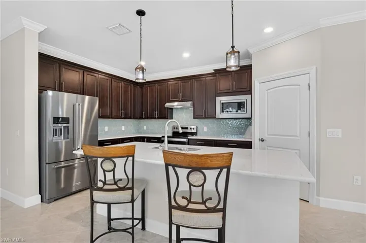 Kitchen featuring dark brown cabinets, stainless steel appliances, hanging light fixtures, a kitchen bar, and a kitchen island with sink