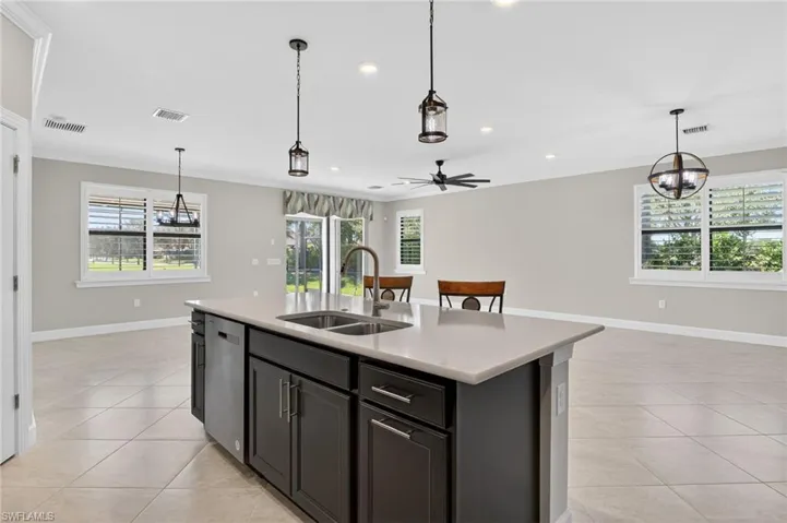 Kitchen with hanging light fixtures, open floor plan, ceiling fan, an island with sink, and a chandelier