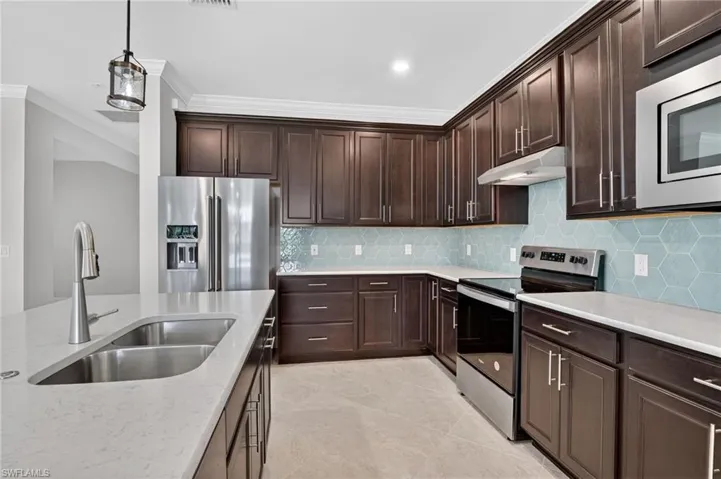 Kitchen with stainless steel appliances, dark brown cabinetry, decorative light fixtures, under cabinet range hood, and ornamental molding