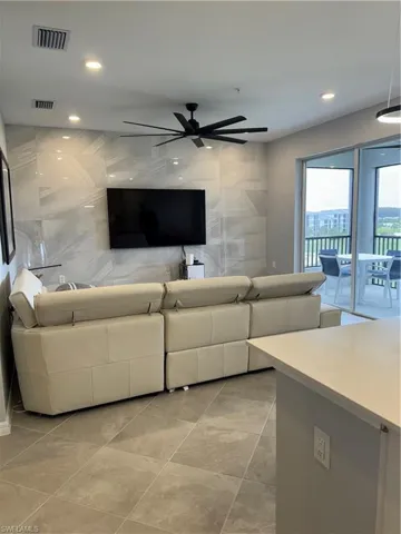 Living room with ceiling fan. Tile finishes on wall.