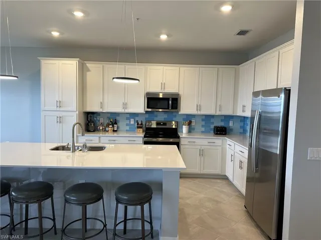 Kitchen with sink, pendant lighting, stainless steel appliances, white cabinets, backsplash and tile finishes.