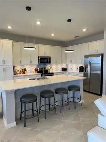 Kitchen with sink, pendant lighting, stainless steel appliances, white cabinets, backsplash and tile finishes.