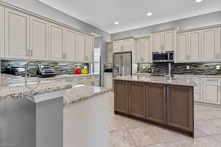 Kitchen with a kitchen island with sink, sink, decorative backsplash, light stone counters, and stainless steel appliances
