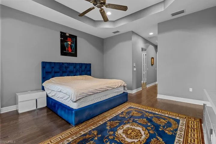 Bedroom with ceiling fan, a raised ceiling, and dark wood-type flooring