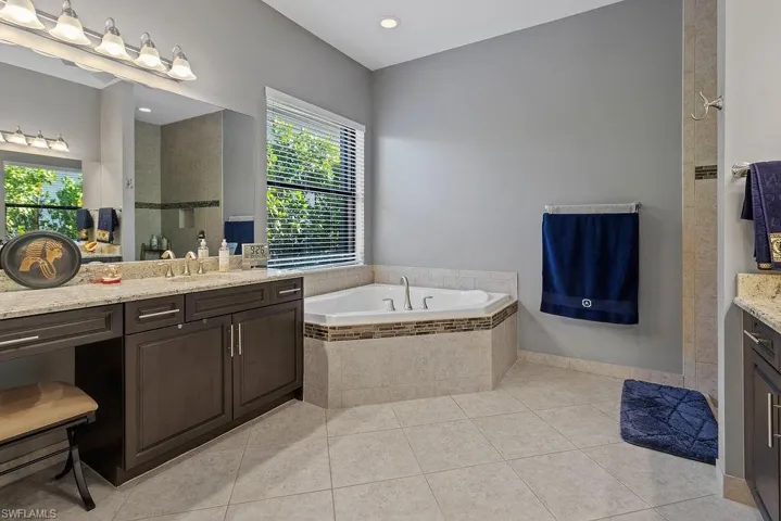 Bathroom with tile patterned flooring, vanity, and a relaxing tiled tub