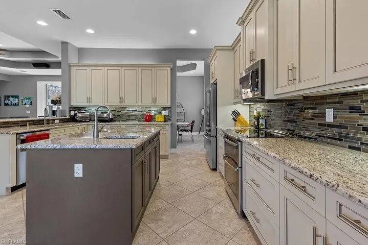 Kitchen with cream cabinets, sink, stainless steel appliances, and an island with sink