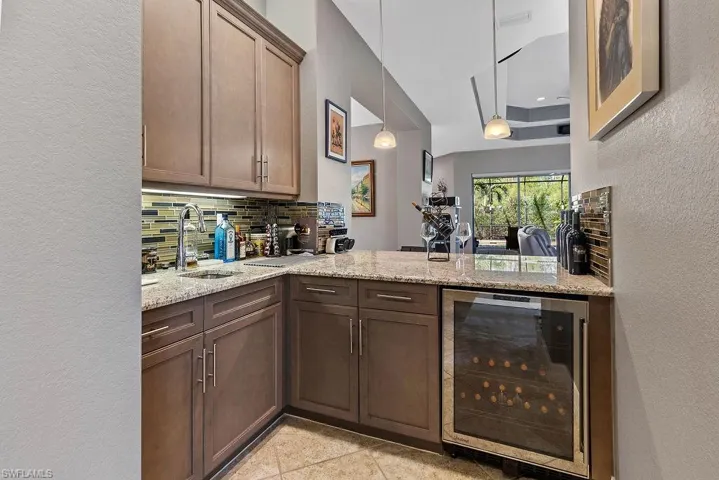 Kitchen with light stone counters, sink, beverage cooler, and tasteful backsplash