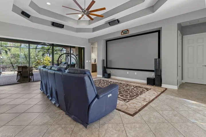 Home theater featuring a tray ceiling, ceiling fan, and light tile patterned floors