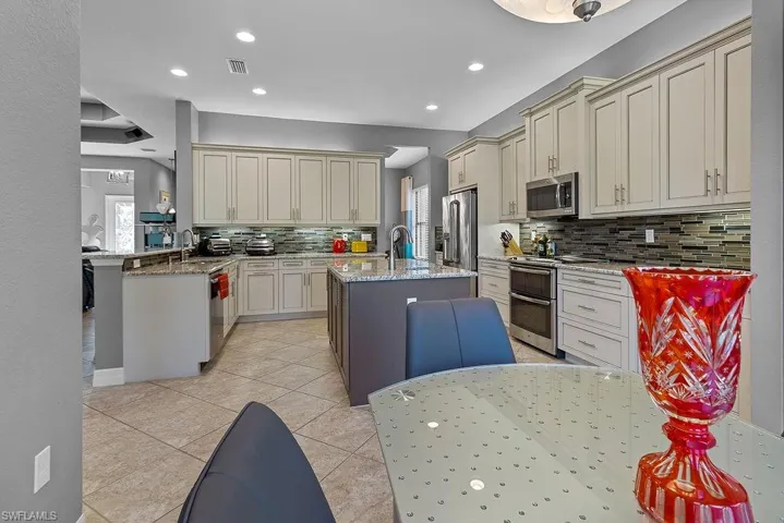Kitchen with backsplash, kitchen peninsula, an island with sink, and stainless steel appliances