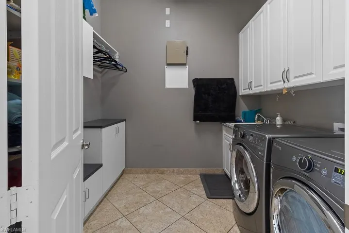 Clothes washing area featuring light tile patterned flooring, cabinets, sink, and washing machine and dryer