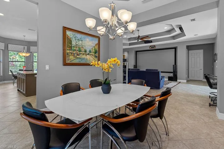 Dining area featuring light tile patterned floors, ceiling fan with notable chandelier, a tray ceiling, and sink