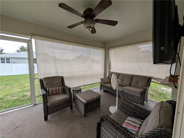 Screened outdoor patio featuring a ceiling fan with light fixture, wall-mounted television, and privacy shades