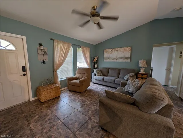 Living area featuring vaulted ceilings, tile flooring, a ceiling fan with light fixture, and multiple windows