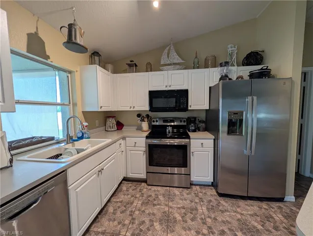 Kitchen featuring white cabinetry, stainless steel appliances, a window above the sink, light-toned countertops, and patterned floor tiling