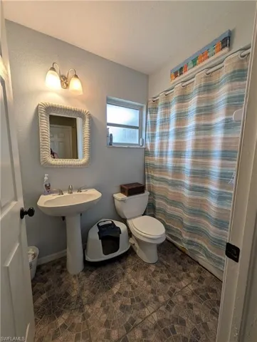 Bathroom featuring a pedestal sink, a toilet, an overhead light fixture, and a window providing natural light