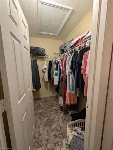 Walk-in closet featuring patterned floor tiles, multiple wire shelving units, and a ceiling access panel