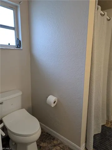 Bathroom featuring a white toilet, textured walls, a frosted window, and patterned tile flooring
