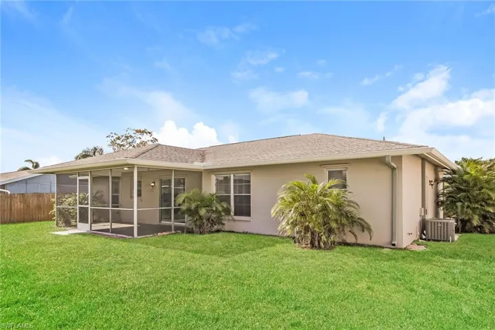 Rear view of house with a sunroom, central AC unit, and a lawn