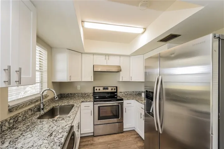 Kitchen with light stone counters, stainless steel appliances, white cabinetry, and sink