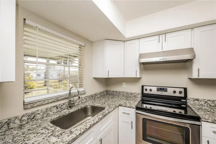 Kitchen featuring white cabinetry, sink, light stone counters, and stainless steel range with electric stovetop