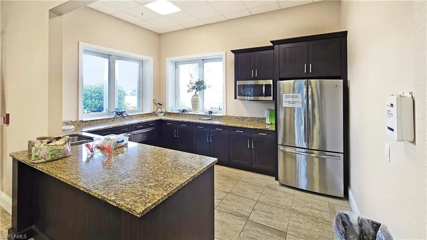 Clubhouse Kitchen with a drop ceiling, light tile patterned floors, light stone counters, kitchen peninsula, and stainless steel appliances