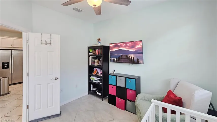 Tiled bedroom featuring stainless steel refrigerator with ice dispenser and ceiling fan