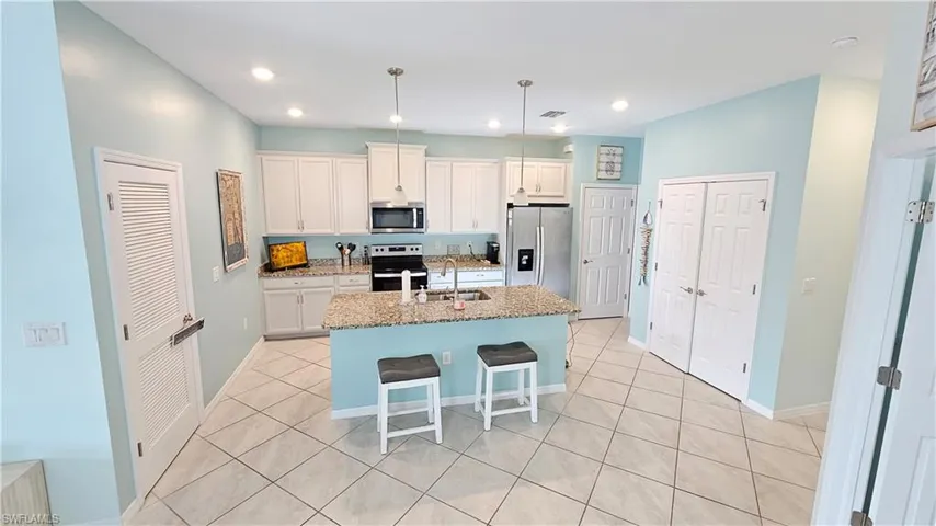 Kitchen with a center island with sink, white cabinets, light stone countertops, and appliances with stainless steel finishes