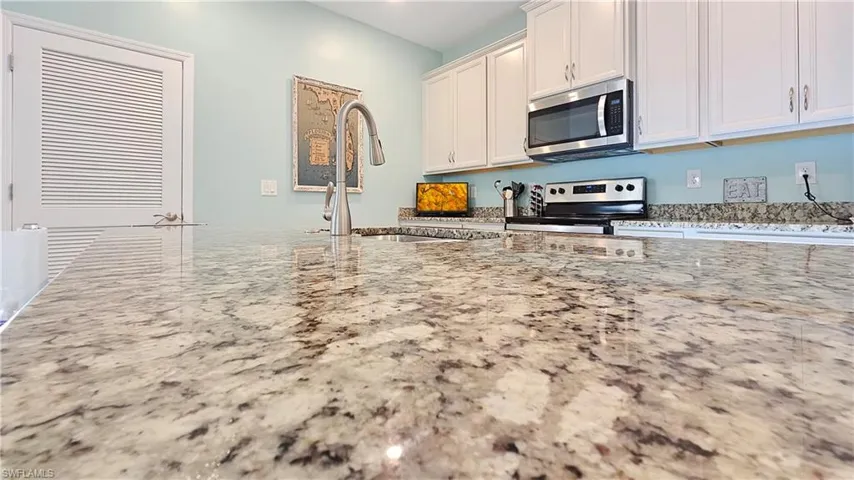 Kitchen with light stone countertops, appliances with stainless steel finishes, white cabinets, and sink