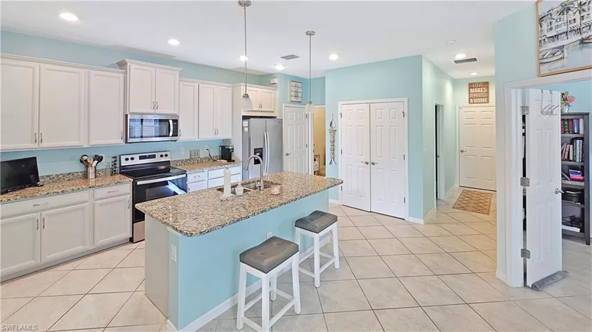 Kitchen with light stone counters, stainless steel appliances, a kitchen island with sink, pendant lighting, and white cabinets