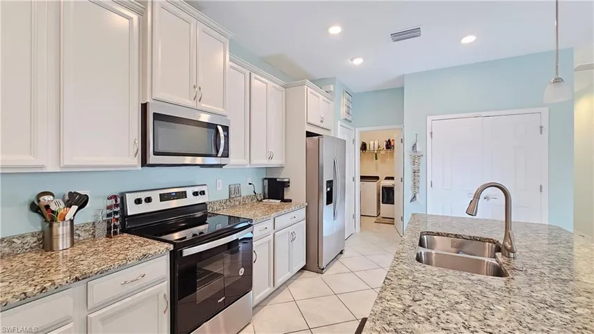 Kitchen featuring light stone countertops, stainless steel appliances, washer and clothes dryer, sink, and white cabinets