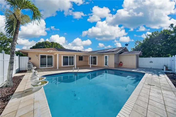 Resort-style pool with a paver patio surround, privacy fencing, and solar panels on the roof