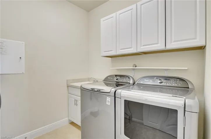 Washroom with light tile patterned flooring, sink, washing machine and clothes dryer, and cabinets