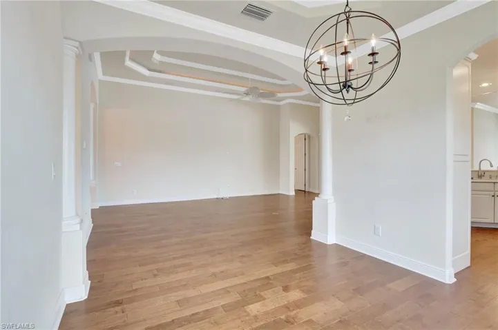 Unfurnished room featuring ceiling fan with notable chandelier, crown molding, light hardwood / wood-style flooring, and a tray ceiling