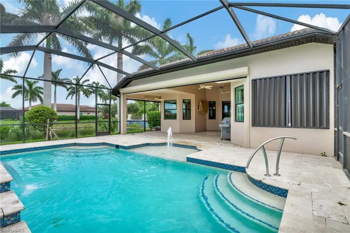 View of swimming pool with ceiling fan, glass enclosure, and pool water feature