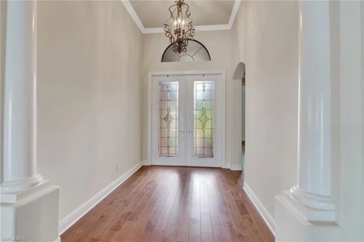 Entrance foyer featuring ornate columns, french doors, hardwood / wood-style flooring, an inviting chandelier, and crown molding