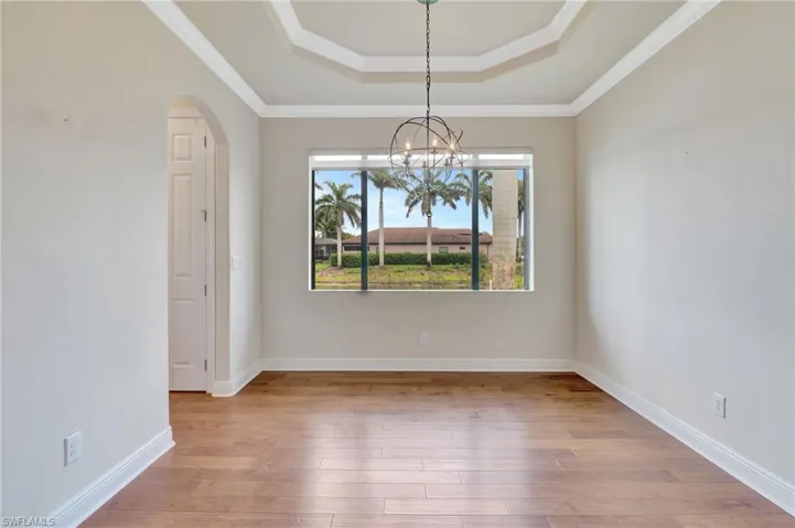 Empty room with light wood-type flooring, a chandelier, ornamental molding, and a tray ceiling