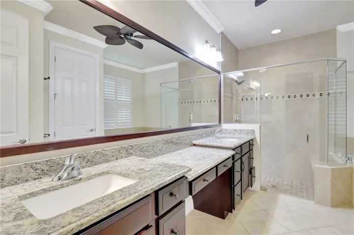 Bathroom featuring ceiling fan, tile patterned flooring, double sink vanity, an enclosed shower, and ornamental molding