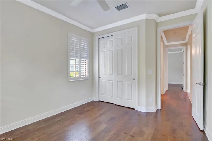 Unfurnished bedroom with ceiling fan, dark hardwood / wood-style floors, ornamental molding, and a closet